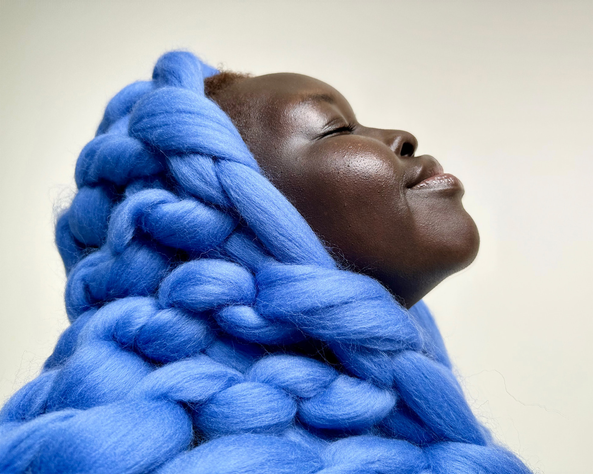 Visage d'une femme souriant de profil avec une capuche de gros noeuds de tissus bleus recouvrant la moitié de son crâne