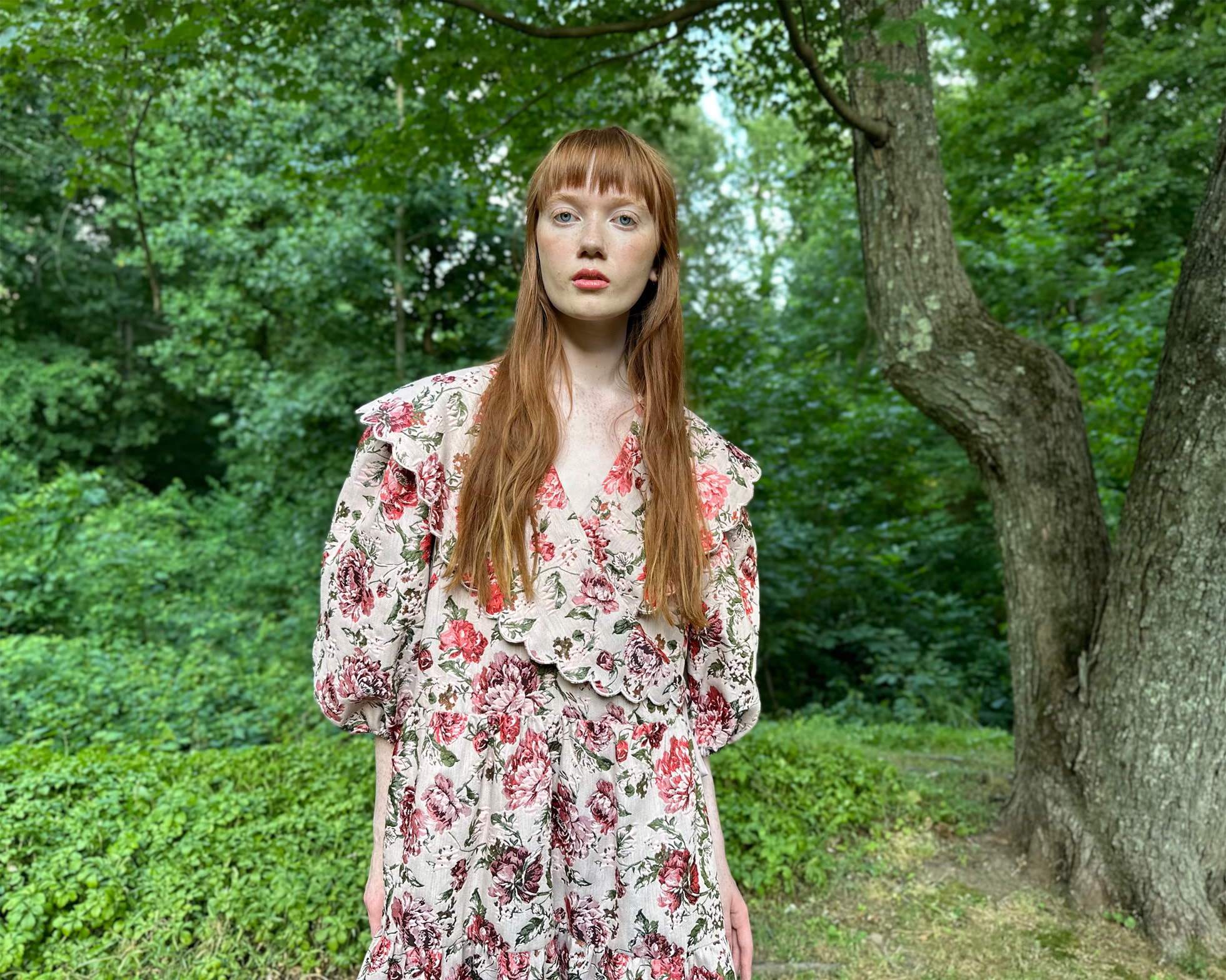 Femme en robe fleurie dans un environnement de verdure à côté d'un arbre