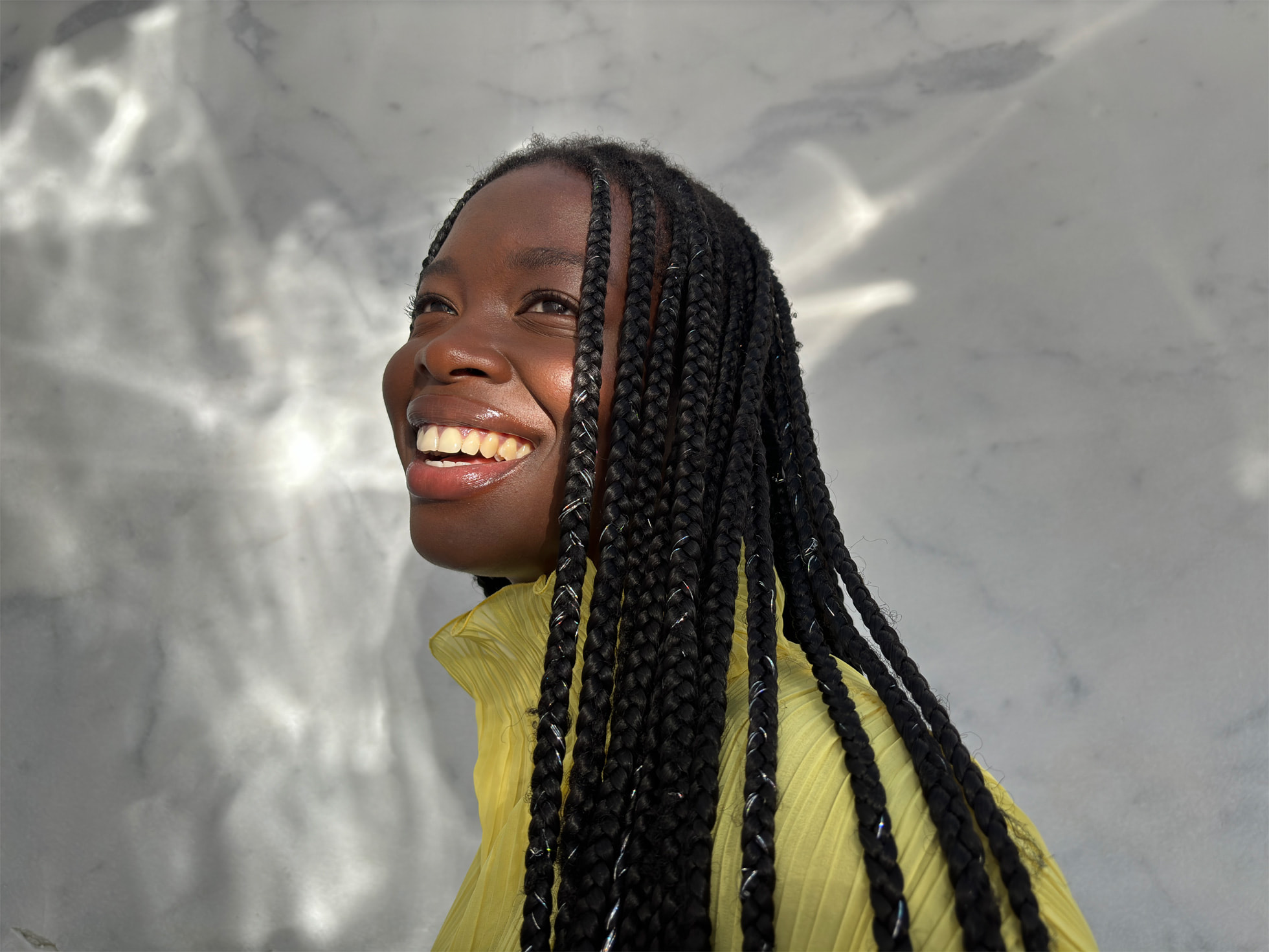 Buste d'une femme de profil souriant, avec en fond un mur d'aluminium