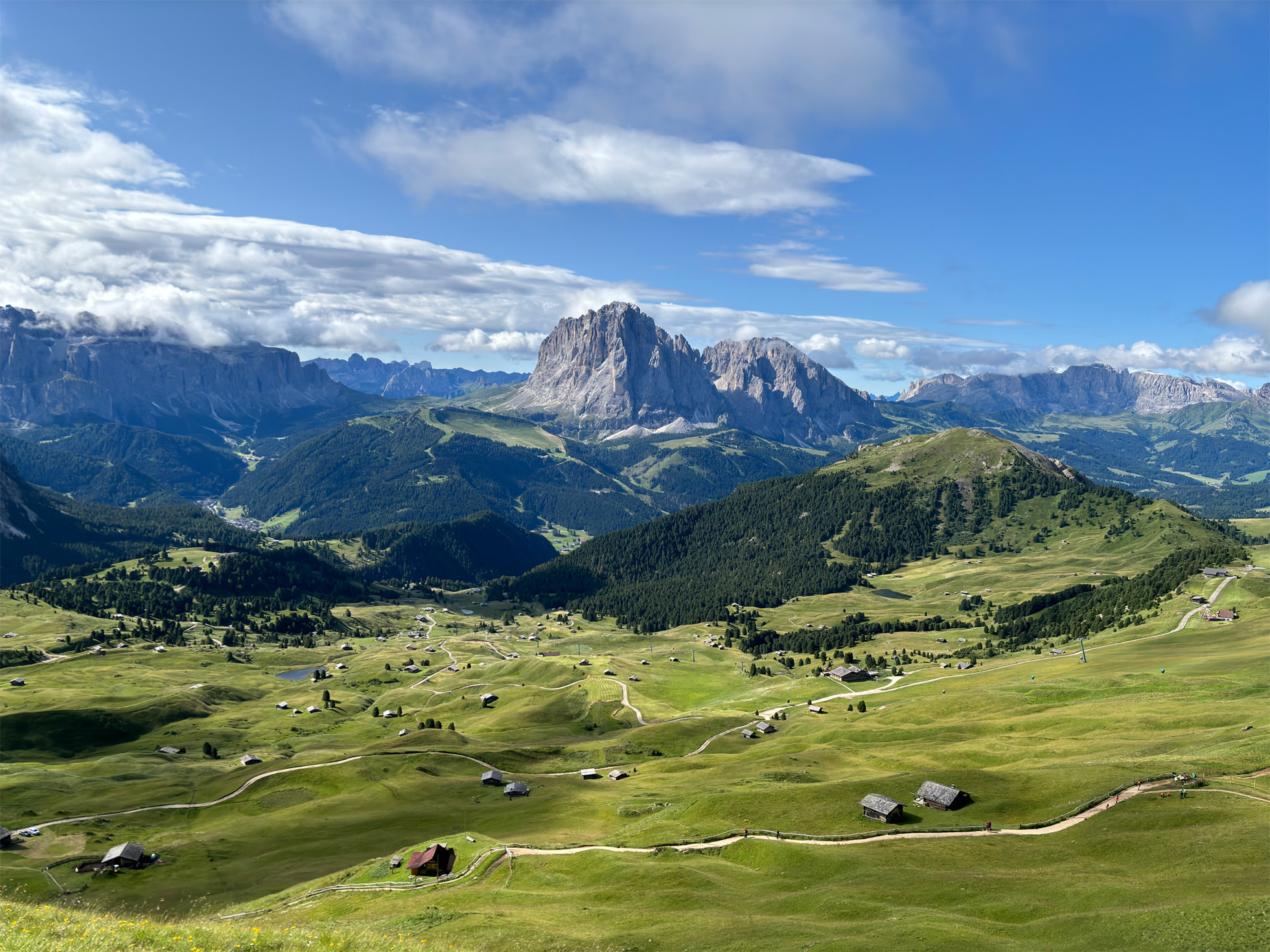 Paysage d'une vallée verdoyante avec, au fond, une chaîne de montagnes qui se détache de l'horizon, ainsi qu'un ciel bleu radieux.