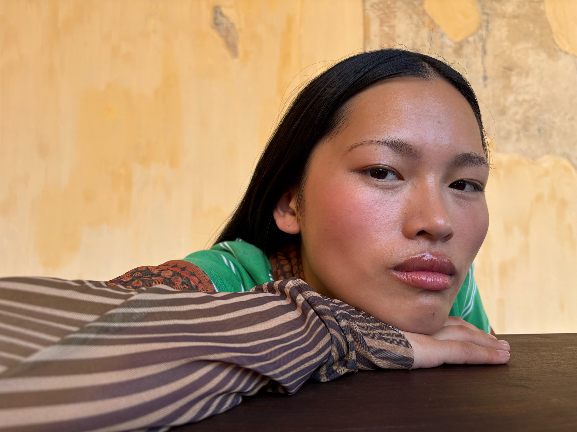 Un portrait en gros plan d’une femme regardant la caméra avec la tête posée sur ses mains.