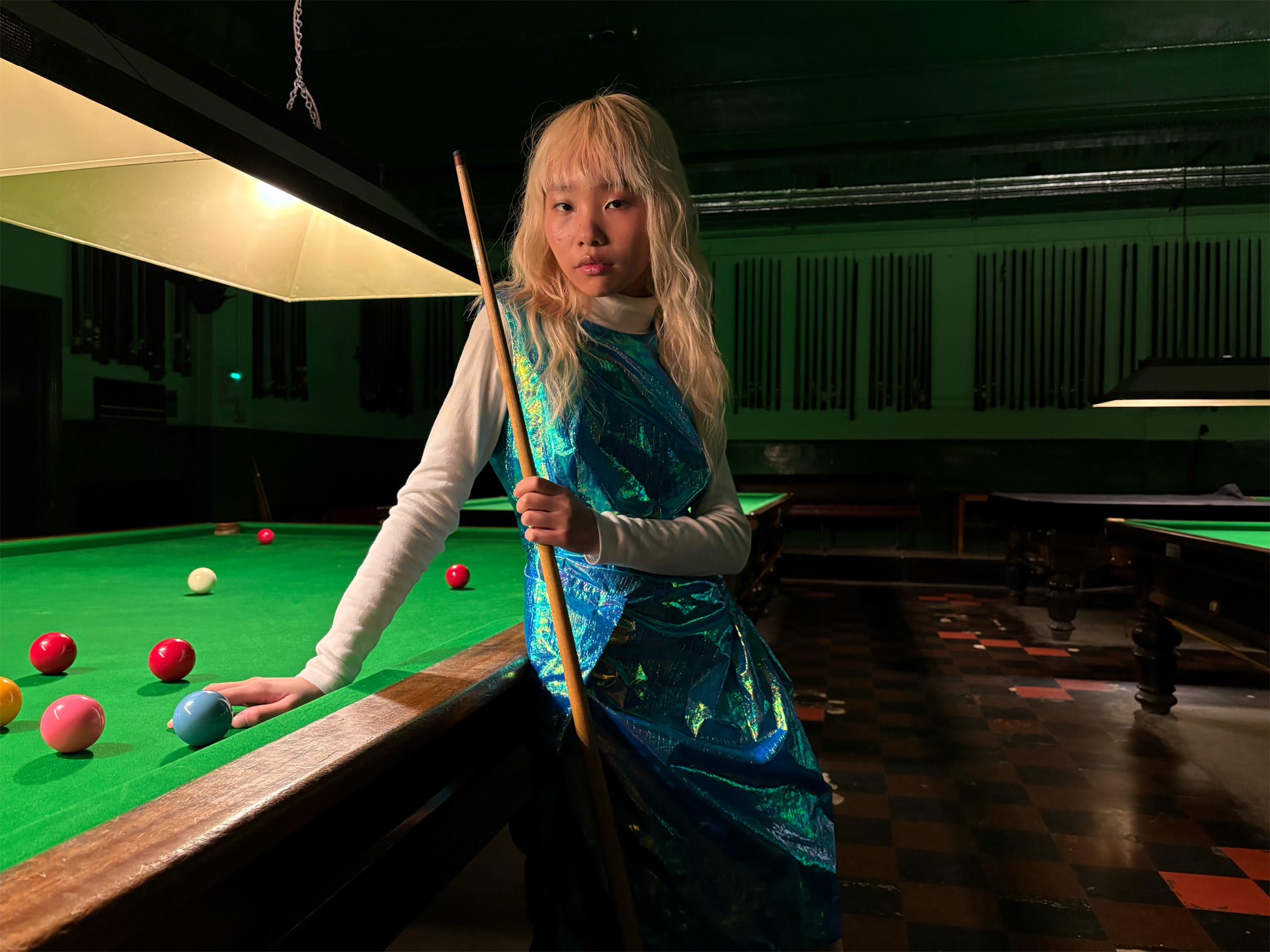 Une femme tenant une queue de billard posée contre une table de billard dans une pièce faiblement éclairée.