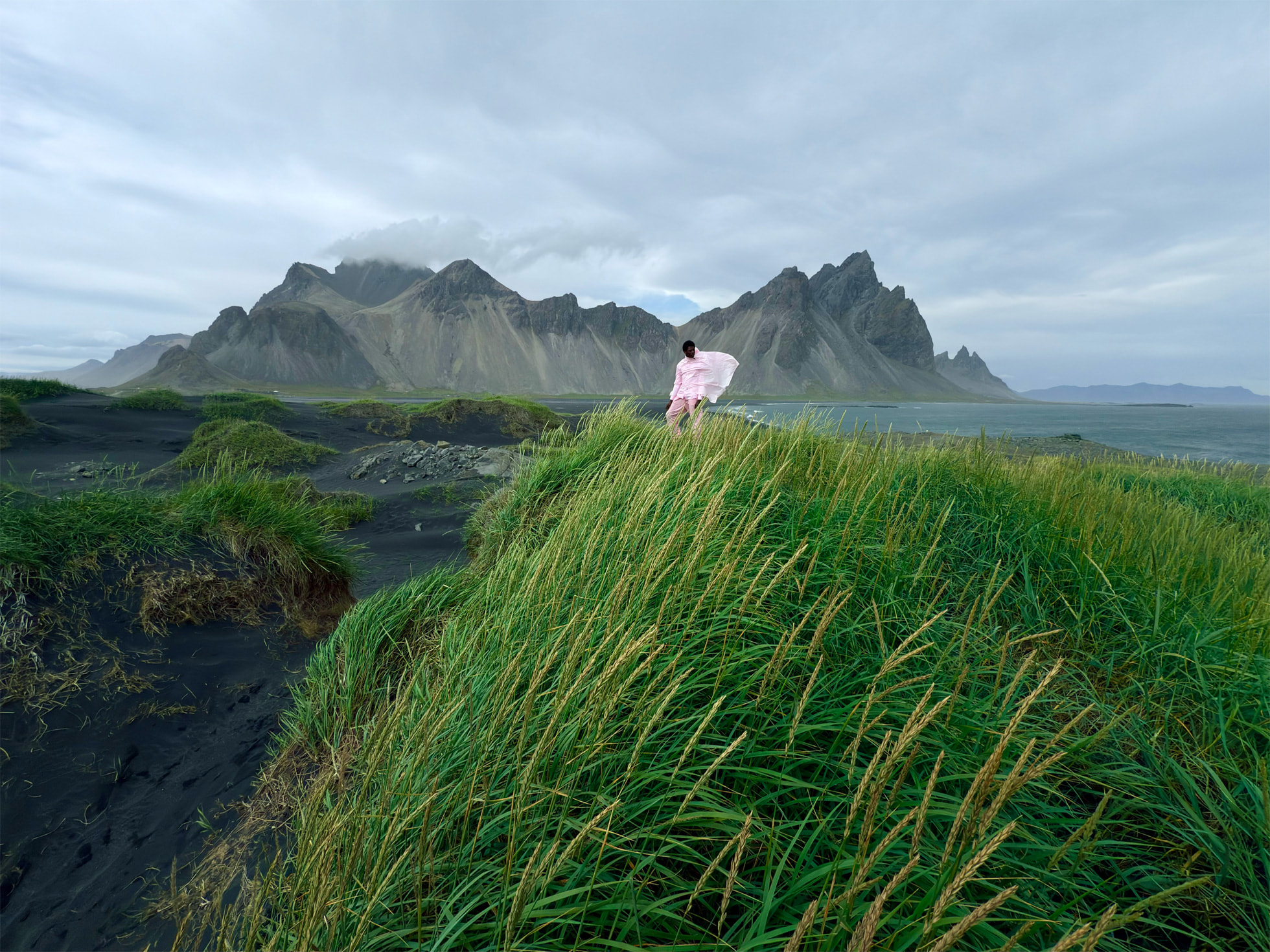 Personne dans des hautes herbes sur un plateau avec une chaîne montagneuse dans le brouillard en fond